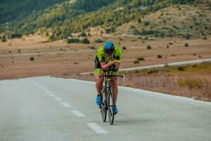 voll Länge Porträt von ein aktiv Triathlet im Sportbekleidung und mit ein schützend Helm Reiten ein Fahrrad. selektiv Fokus foto