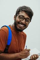 indisch Schüler mit Blau Rucksack, Brille und Notizbuch posieren auf grau Hintergrund. das Konzept von Bildung und Schulung. Zeit zu gehen zurück zu Schule foto
