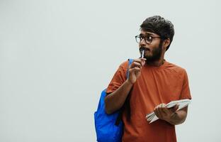 verwirrt indisch Schüler mit Blau Rucksack, Brille und Notizbuch posieren auf grau Hintergrund. das Konzept von Bildung und Schulung. Zeit zu gehen zurück zu Schule foto