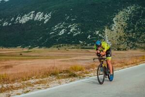 voll Länge Porträt von ein aktiv Triathlet im Sportbekleidung und mit ein schützend Helm Reiten ein Fahrrad. selektiv Fokus foto