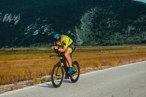 voll Länge Porträt von ein aktiv Triathlet im Sportbekleidung und mit ein schützend Helm Reiten ein Fahrrad. selektiv Fokus foto