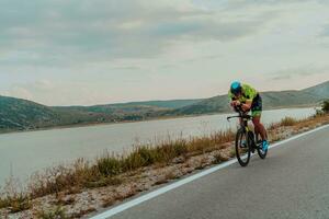 voll Länge Porträt von ein aktiv Triathlet im Sportbekleidung und mit ein schützend Helm Reiten ein Fahrrad. selektiv Fokus foto