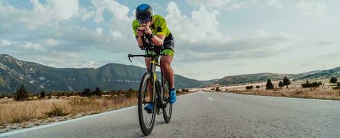 voll Länge Porträt von ein aktiv Triathlet im Sportbekleidung und mit ein schützend Helm Reiten ein Fahrrad. selektiv Fokus foto