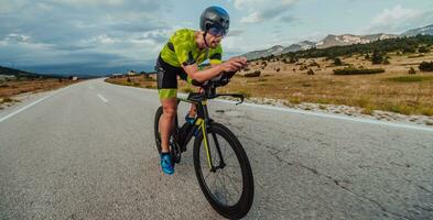 voll Länge Porträt von ein aktiv Triathlet im Sportbekleidung und mit ein schützend Helm Reiten ein Fahrrad. selektiv Fokus foto