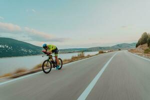 voll Länge Porträt von ein aktiv Triathlet im Sportbekleidung und mit ein schützend Helm Reiten ein Fahrrad. selektiv Fokus foto