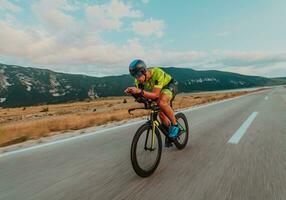 voll Länge Porträt von ein aktiv Triathlet im Sportbekleidung und mit ein schützend Helm Reiten ein Fahrrad. selektiv Fokus foto