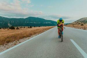 voll Länge Porträt von ein aktiv Triathlet im Sportbekleidung und mit ein schützend Helm Reiten ein Fahrrad. selektiv Fokus foto