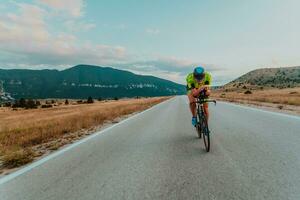 voll Länge Porträt von ein aktiv Triathlet im Sportbekleidung und mit ein schützend Helm Reiten ein Fahrrad. selektiv Fokus foto