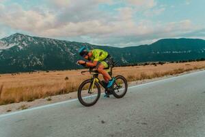 voll Länge Porträt von ein aktiv Triathlet im Sportbekleidung und mit ein schützend Helm Reiten ein Fahrrad. selektiv Fokus foto