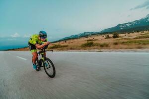 voll Länge Porträt von ein aktiv Triathlet im Sportbekleidung und mit ein schützend Helm Reiten ein Fahrrad. selektiv Fokus foto