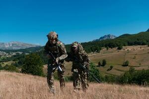 ein Scharfschütze Mannschaft Kader von Soldaten ist gehen verdeckt. Scharfschütze Assistent und Mannschaft Führer Gehen und Zielen im Natur mit Gelb Gras und Blau Himmel. taktisch tarnen Uniform. foto