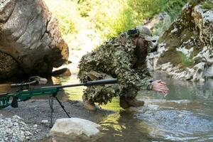 Soldat im ein tarnen passen Uniform Trinken frisch Wasser von das Fluss. Militär- Scharfschütze Gewehr auf das Seite. foto
