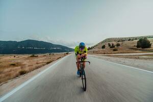 voll Länge Porträt von ein aktiv Triathlet im Sportbekleidung und mit ein schützend Helm Reiten ein Fahrrad. selektiv Fokus foto