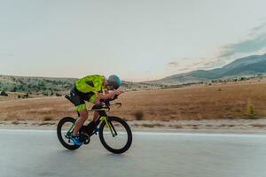 voll Länge Porträt von ein aktiv Triathlet im Sportbekleidung und mit ein schützend Helm Reiten ein Fahrrad. selektiv Fokus foto