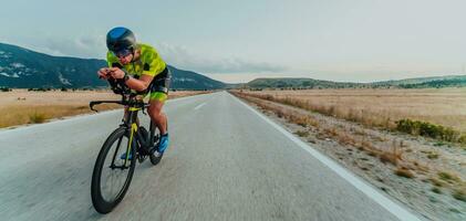 voll Länge Porträt von ein aktiv Triathlet im Sportbekleidung und mit ein schützend Helm Reiten ein Fahrrad. selektiv Fokus foto