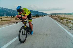 voll Länge Porträt von ein aktiv Triathlet im Sportbekleidung und mit ein schützend Helm Reiten ein Fahrrad. selektiv Fokus foto