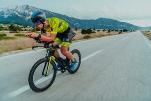 voll Länge Porträt von ein aktiv Triathlet im Sportbekleidung und mit ein schützend Helm Reiten ein Fahrrad. selektiv Fokus foto