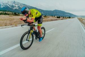 voll Länge Porträt von ein aktiv Triathlet im Sportbekleidung und mit ein schützend Helm Reiten ein Fahrrad. selektiv Fokus foto