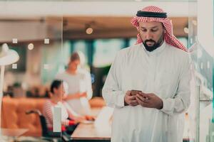 Mitte östlichen arabisch Geschäftsmann im das Büro Sprechen auf Smartphone im Vorderseite von seine Mannschaft foto