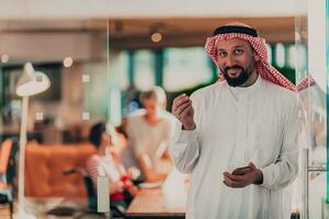 Mitte östlichen arabisch Geschäftsmann im das Büro Sprechen auf Smartphone im Vorderseite von seine Mannschaft foto
