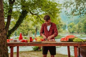 ein Mann vorbereiten ein köstlich Abendessen zum seine freunde Wer sind haben Spaß durch das Fluss im Natur foto