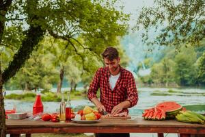ein Mann vorbereiten ein köstlich Abendessen zum seine freunde Wer sind haben Spaß durch das Fluss im Natur foto