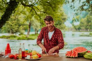 ein Mann vorbereiten ein köstlich Abendessen zum seine freunde Wer sind haben Spaß durch das Fluss im Natur foto