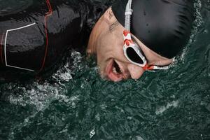 Triathlon-Athlet, der auf dem See schwimmt und einen Neoprenanzug trägt foto
