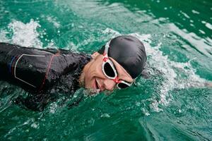 Triathlon-Athlet, der auf dem See schwimmt und einen Neoprenanzug trägt foto