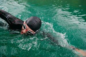 Triathlon-Athlet, der auf dem See schwimmt und einen Neoprenanzug trägt foto