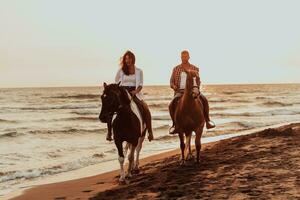 Ein liebevolles Paar in Sommerkleidung, das bei Sonnenuntergang an einem Sandstrand reitet. Meer und Sonnenuntergang im Hintergrund. selektiver Fokus foto