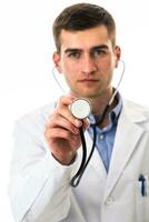 Porträt von Held im ein Weiß Mantel. heiter lächelnd jung Arzt mit ein Stethoskop im ein medizinisch Krankenhaus Stehen gegen ein Weiß Hintergrund. Coronavirus covid-19 Achtung warnen foto
