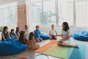 ein glücklich weiblich Lehrer Sitzung und spielen Hand Spiele mit ein Gruppe von wenig Schulkinder foto