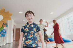 klein Kindergarten Schule Kinder mit weiblich Lehrer auf Fußboden drinnen im Klassenzimmer, tun Übung. Springen Über Hula Band Kreise Spur auf das Boden. foto