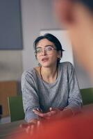 im ein modern Büro, ein jung Lächeln Geschäftsfrau mit Brille selbstbewusst erklärt und die Geschenke verschiedene Geschäft Ideen zu ihr Kollegen, präsentieren ihr Professionalität und Sachverstand. foto