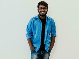 indisch lächelnd jung Mann mit Blau Hemd und Brille posieren auf grau Hintergrund foto