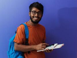 indisch Schüler mit Blau Rucksack, Brille und Notizbuch posieren auf lila Hintergrund. das Konzept von Bildung und Schulung. Zeit zu gehen zurück zu Schule foto