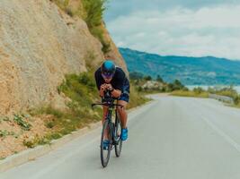 voll Länge Porträt von ein aktiv Triathlet im Sportbekleidung und mit ein schützend Helm Reiten ein Fahrrad. selektiv Fokus foto