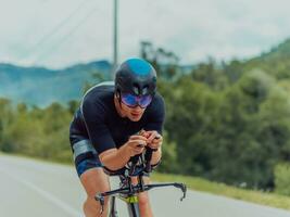 voll Länge Porträt von ein aktiv Triathlet im Sportbekleidung und mit ein schützend Helm Reiten ein Fahrrad. selektiv Fokus foto