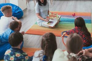 ein glücklich weiblich Lehrer Sitzung und spielen Hand Spiele mit ein Gruppe von wenig Schulkinder foto