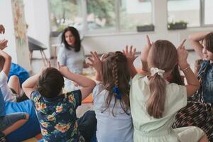 ein glücklich weiblich Lehrer Sitzung und spielen Hand Spiele mit ein Gruppe von wenig Schulkinder foto