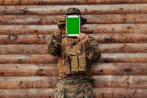 Soldat mit Tablette Computer gegen alt hölzern Mauer im Militär- Lager zu bleibe im Kontakt mit freunde und Familie foto