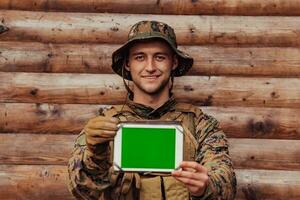 Soldat mit Tablette Computer gegen alt hölzern Mauer im Militär- Lager zu bleibe im Kontakt mit freunde und Familie foto