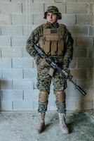 ein Soldat im Uniform steht im Vorderseite von ein Stein Mauer im voll Krieg Ausrüstung vorbereiten zum Schlacht foto