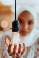 sentimental Porträt von Afroamerikaner jung weiblich Muslim tragen Hijab während halten ein die Glühbirne. foto