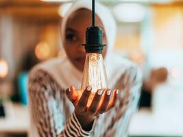 sentimental Porträt von Afroamerikaner jung weiblich Muslim tragen Hijab während halten ein die Glühbirne. foto