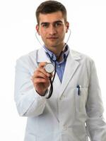 Porträt von Held im ein Weiß Mantel. heiter lächelnd jung Arzt mit ein Stethoskop im ein medizinisch Krankenhaus Stehen gegen ein Weiß Hintergrund. Coronavirus covid-19 Achtung warnen foto