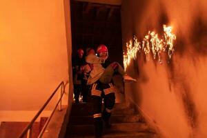 mutig Feuerwehrmann sinkt ab Treppe von ein Verbrennung Gebäude und hält Gerettet Mädchen im seine Waffen. öffnen Feuer und einer Feuerwehrmann im das Hintergrund. foto