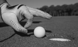 Die Hand des Mannes, die den Golfball in das Loch steckt foto