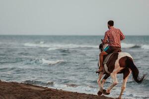 ein moderner mann in sommerkleidung genießt es, bei sonnenuntergang an einem schönen sandstrand zu reiten. selektiver Fokus foto